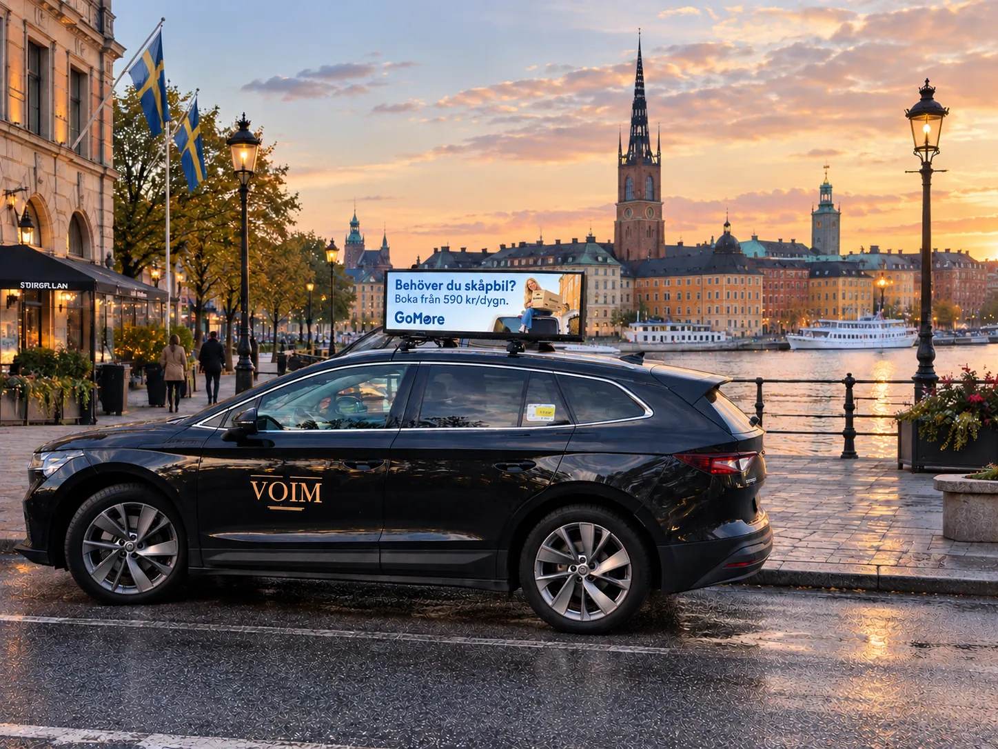 Svart bil med digital GoMore-takskylt vid vattnet i Stockholm i kvällsljus